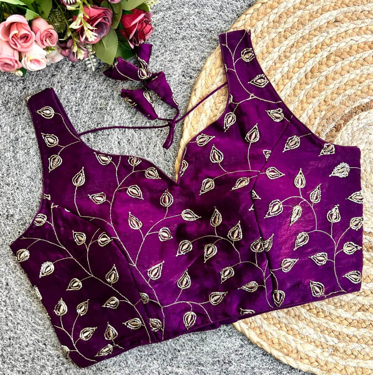 Purple saree with gold patterns on a textured surface with flowers and a woven mat.