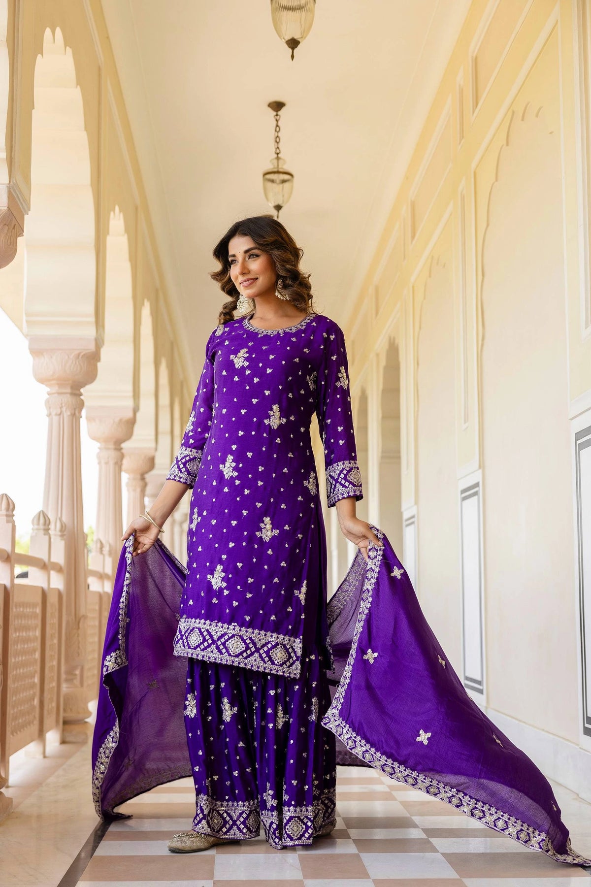 Woman in a purple traditional outfit standing in an elegant hallway.