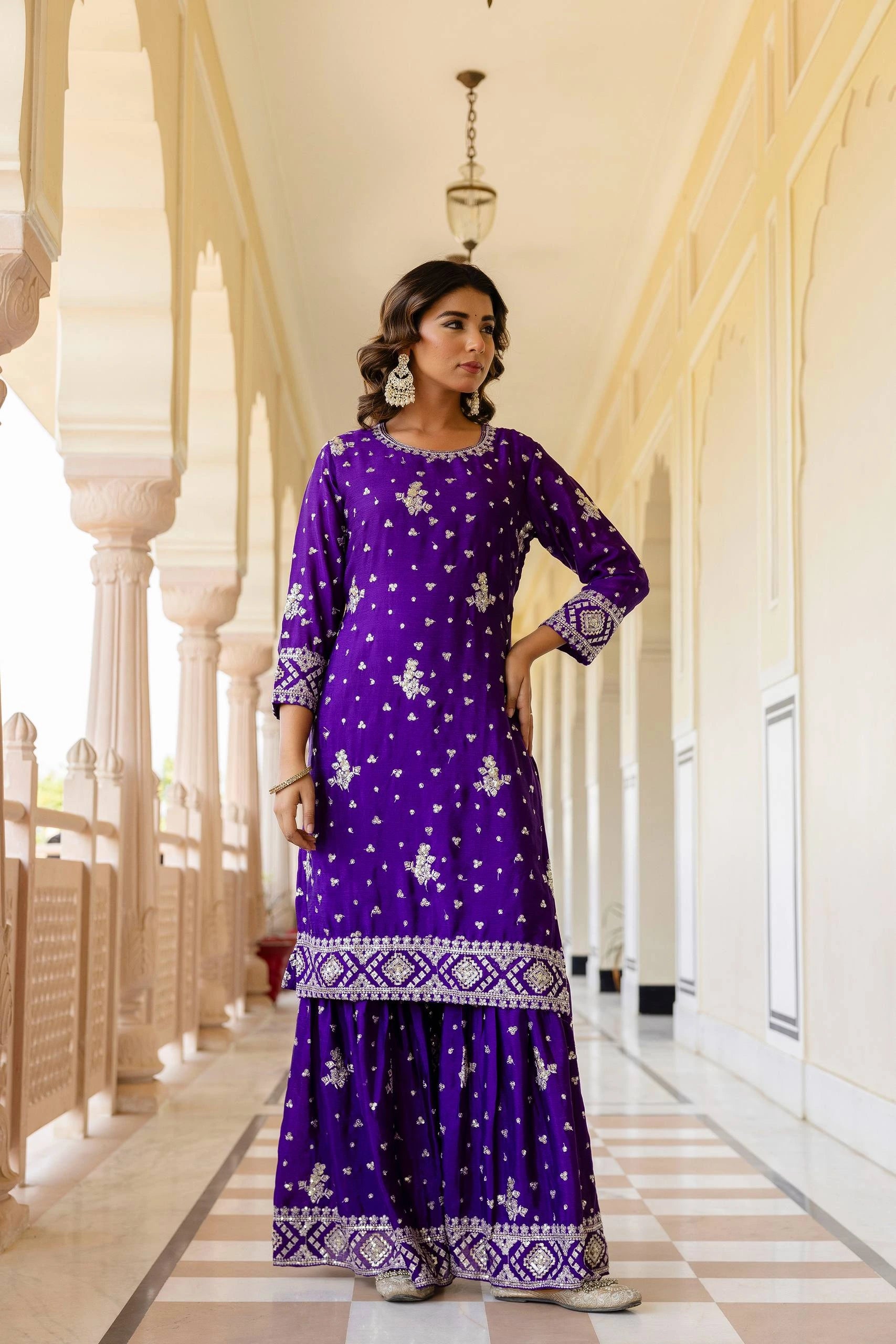 Woman in a purple traditional outfit standing in a decorative hallway.
