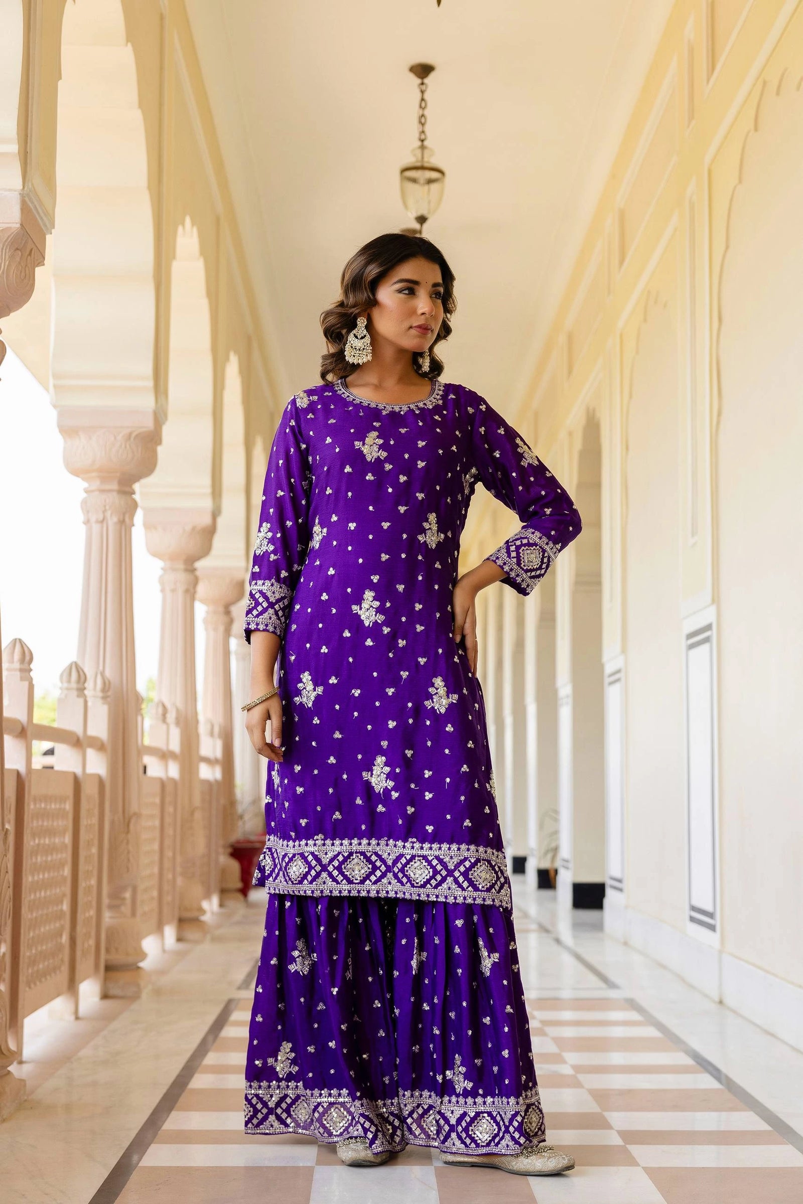 Woman in a purple traditional outfit standing in a decorative hallway.