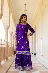 Woman in a purple traditional outfit standing in a decorative hallway.