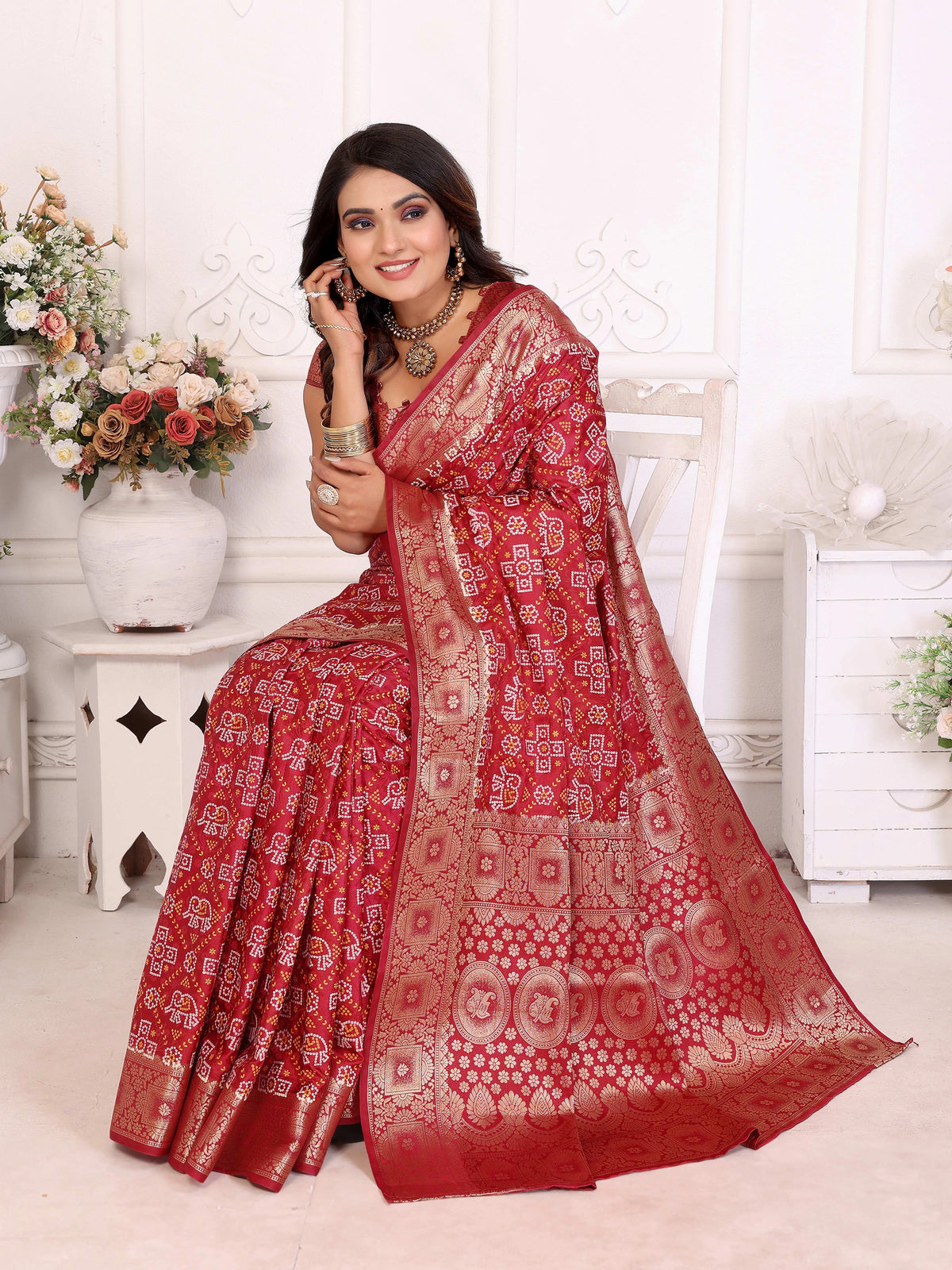 Woman wearing a red saree with white patterns in a decorated room.