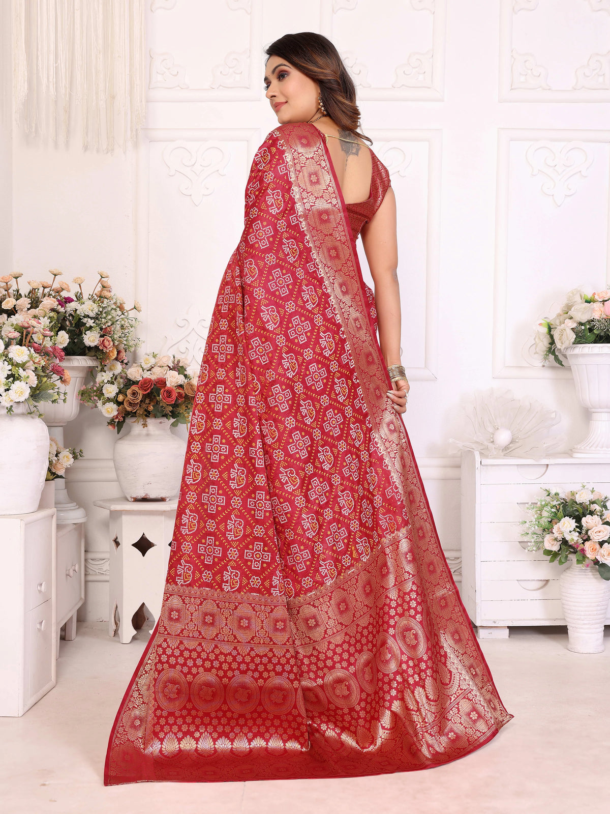 Woman wearing a red saree with white patterns in a decorated room.
