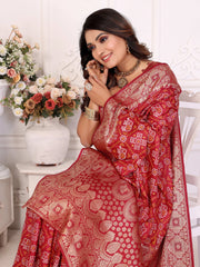 Woman wearing a red saree with white patterns, sitting indoors with flowers in the background.