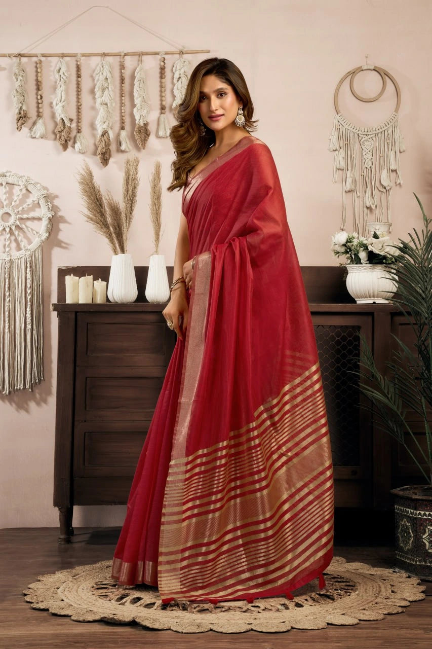 Woman in a red saree with a striped pattern standing in a room with decorative elements.