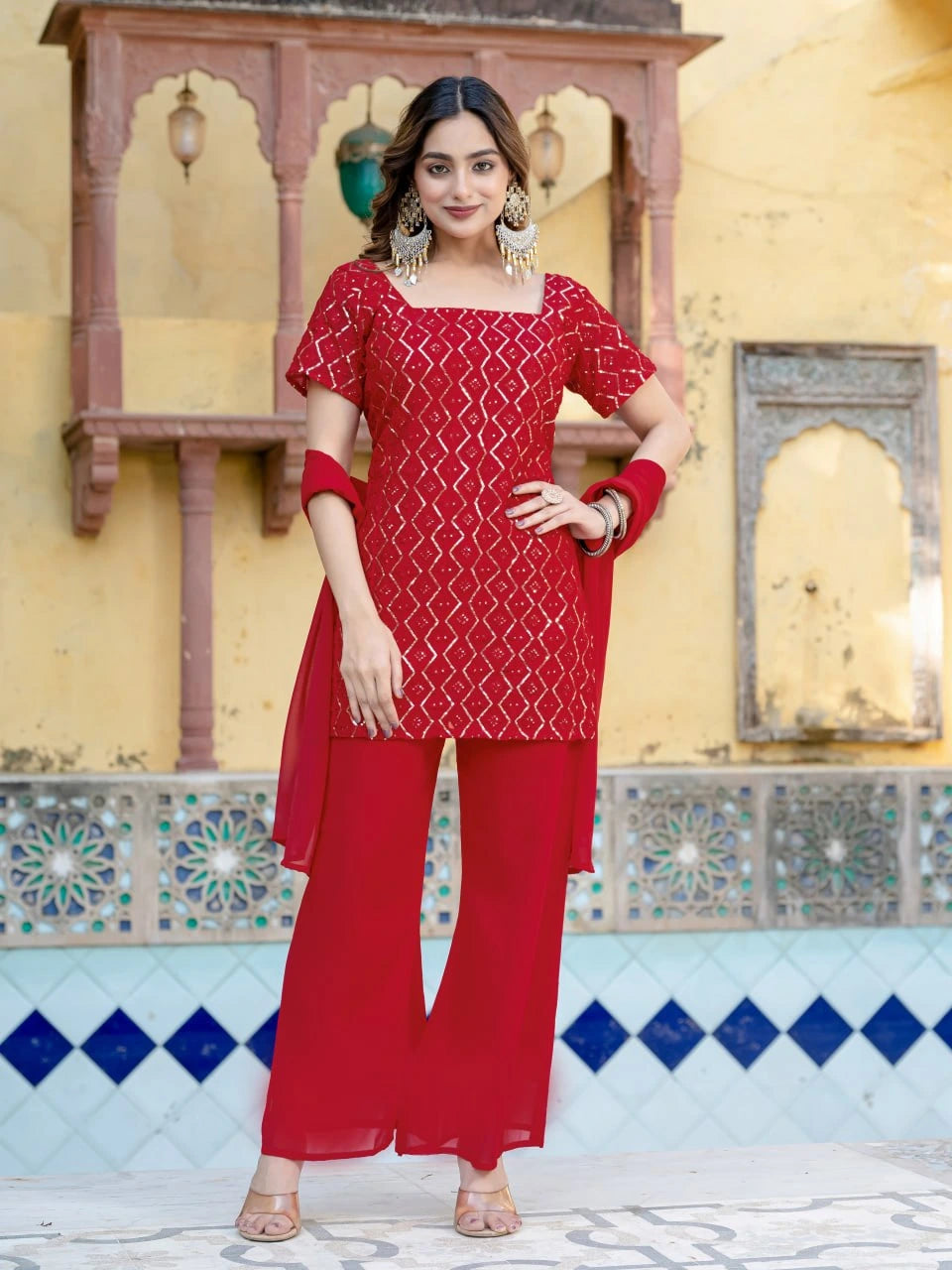Woman in a red traditional outfit standing in front of a decorative wall.