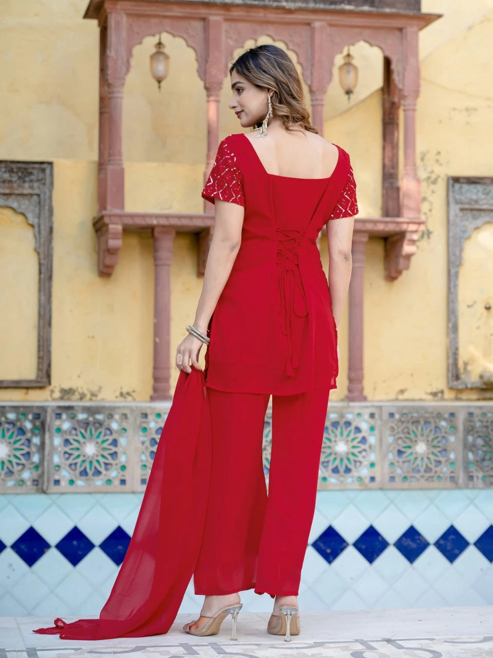 Woman in a red outfit standing in front of a decorative wall with geometric patterns.
