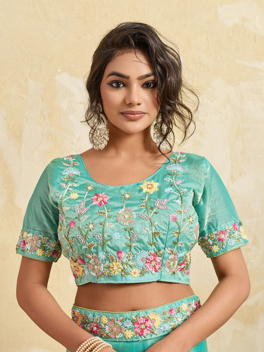Woman wearing a teal blouse with floral embroidery on a beige background