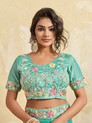 Woman wearing a teal blouse with floral embroidery on a beige background