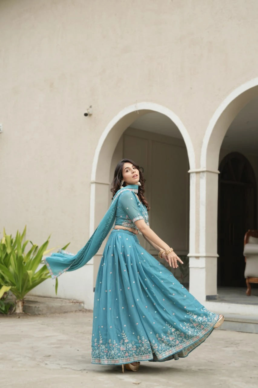 Woman in a blue traditional outfit standing in front of a beige wall with arches.