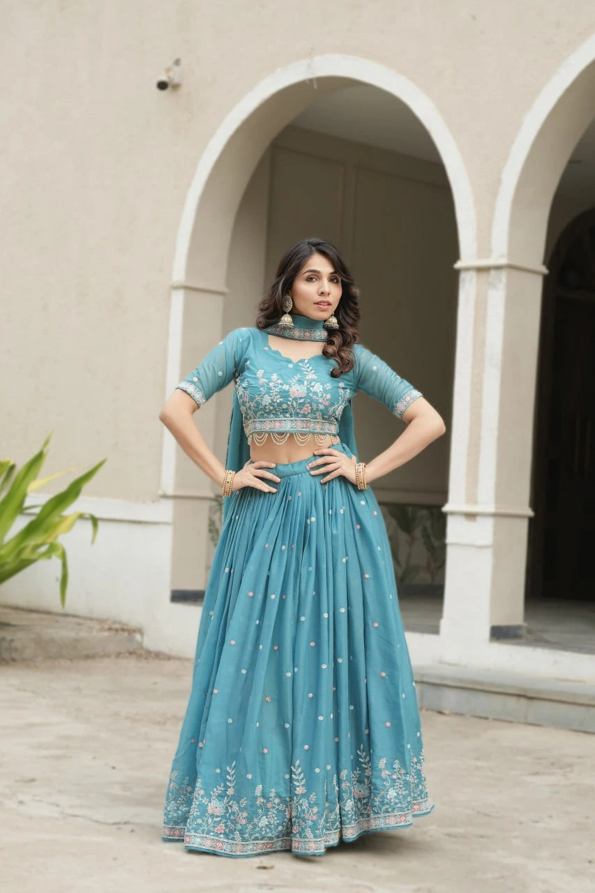 Woman in a teal traditional outfit standing in front of architectural arches.