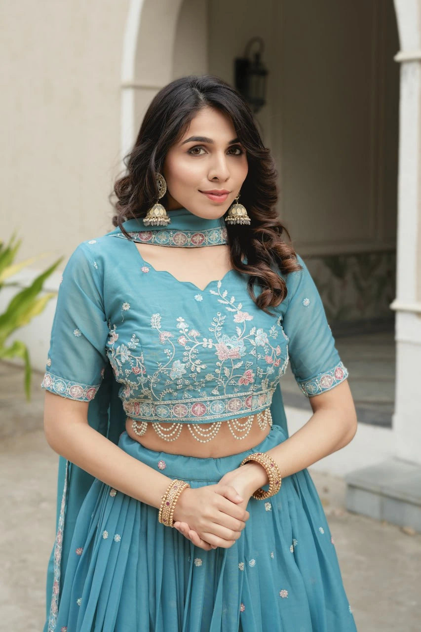 Woman wearing a traditional teal outfit with floral patterns in an outdoor setting.