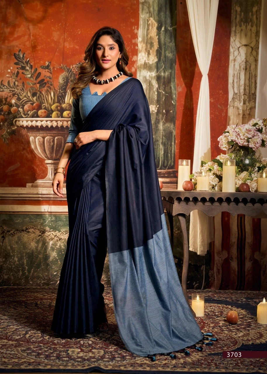 Woman in a navy blue and gray saree standing in an elegant room with decorative elements.