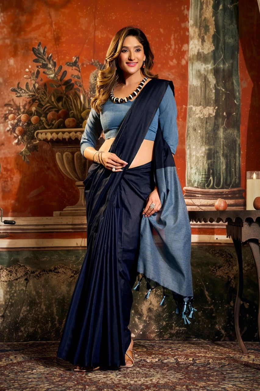 Woman in a blue saree standing in an elegant indoor setting with decorative elements.