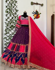 Colorful traditional outfit with a purple and pink lehenga and blouse on a mannequin against a decorative wall.