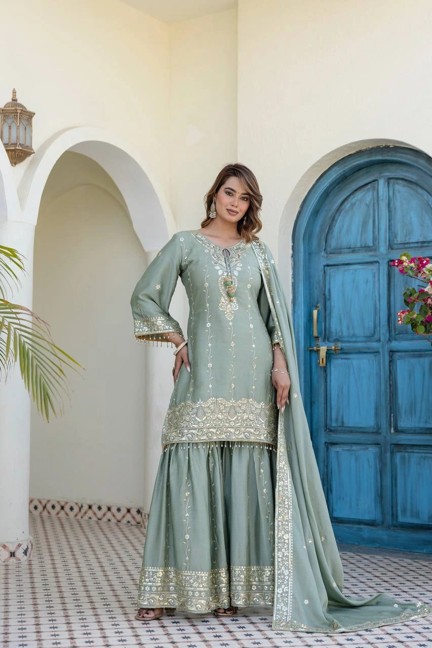 Woman in a light green traditional outfit with gold embroidery standing in front of a blue door.