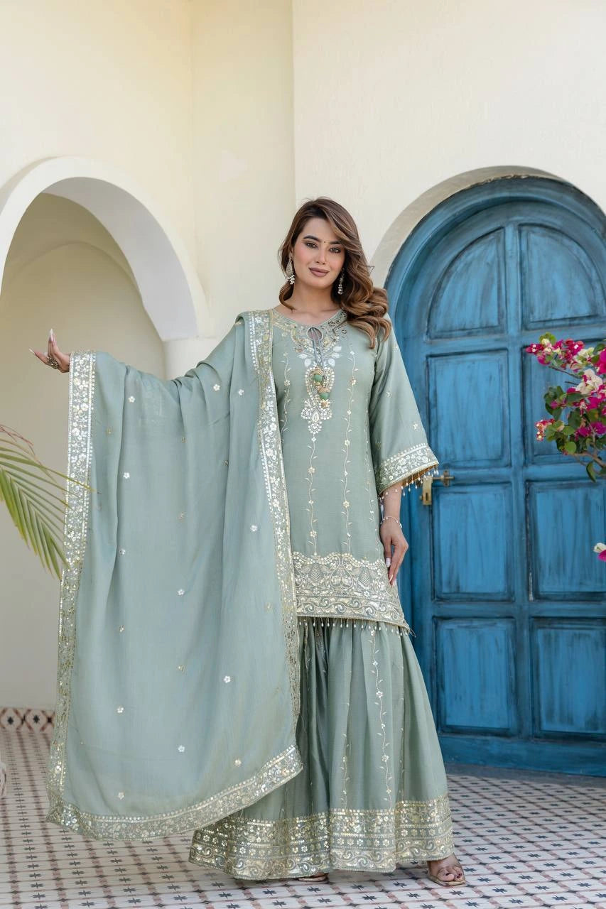 Woman in a traditional outfit with intricate designs standing in front of a blue door.