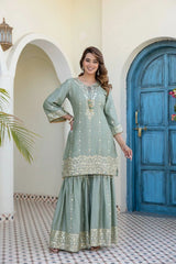 Woman in a light blue embroidered dress standing in front of a blue door.