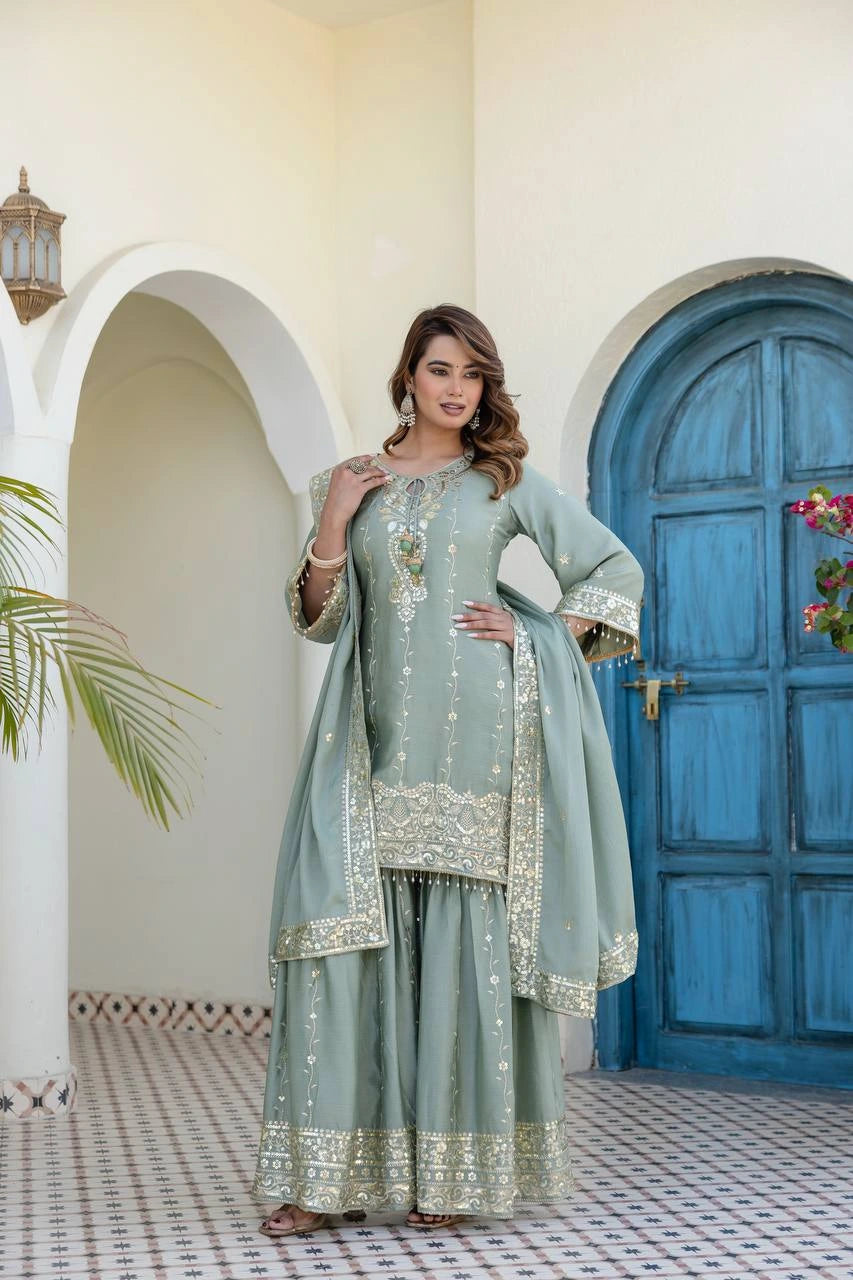 Woman in a light blue embroidered traditional outfit standing in front of a blue door.