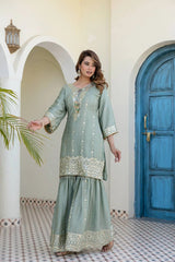 Woman in a light green traditional outfit standing in a decorative outdoor setting with a blue door and white archway.