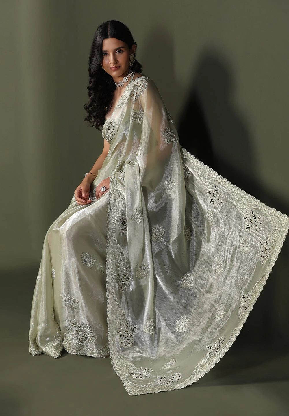 Woman wearing a white saree with intricate designs on a plain background