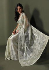 Woman wearing a white saree with intricate designs on a plain background