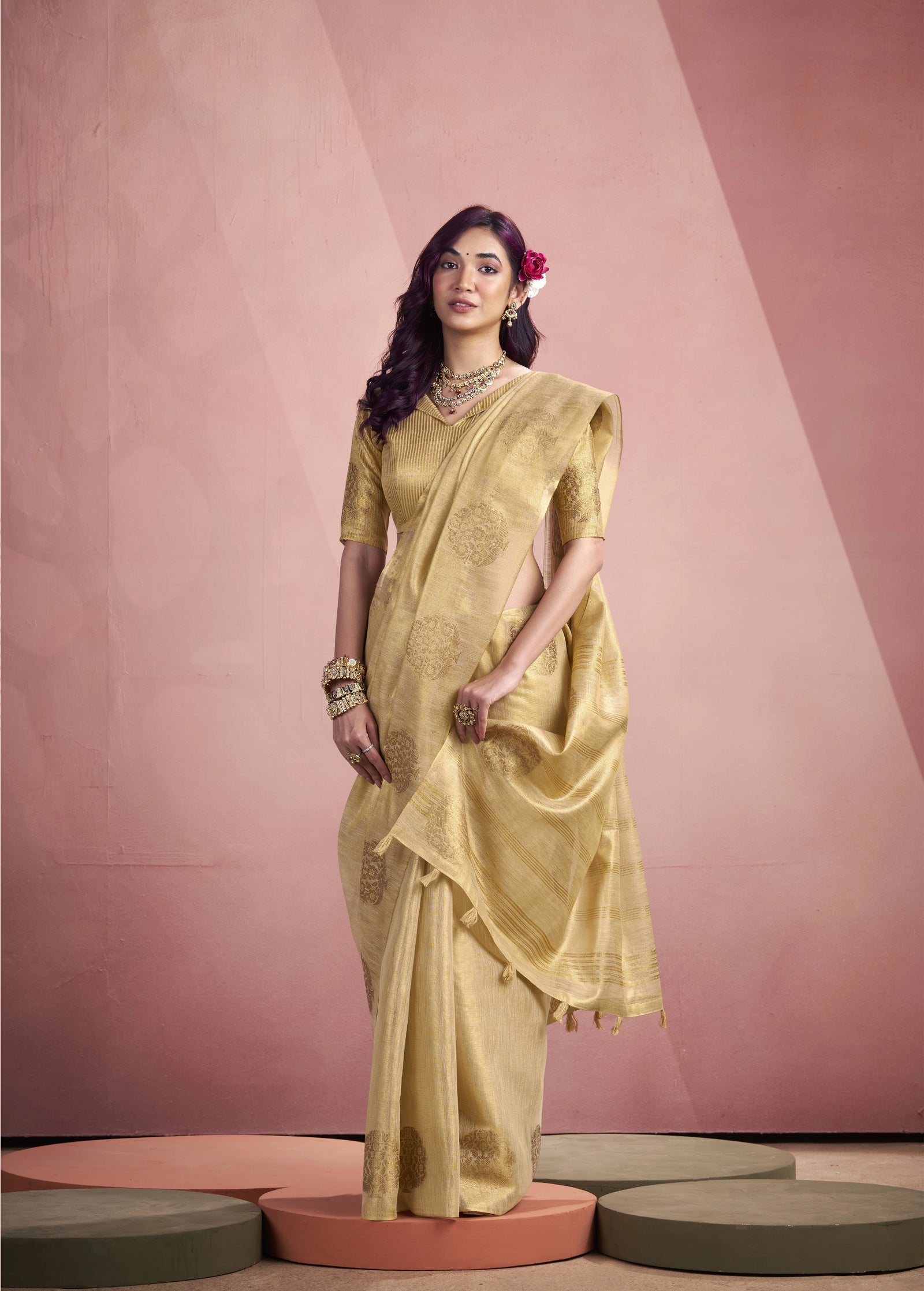 Woman in a yellow saree standing against a pink background