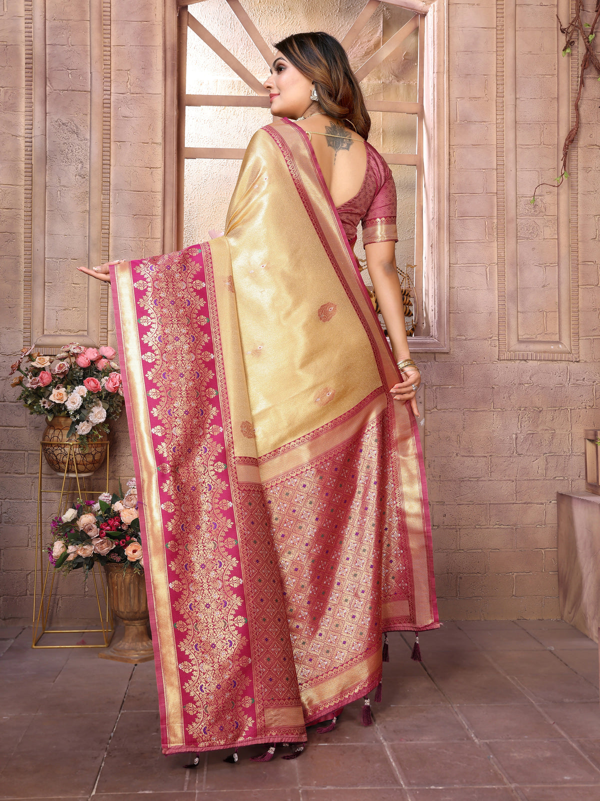 Woman wearing a traditional saree with a decorative border in a decorated indoor setting.