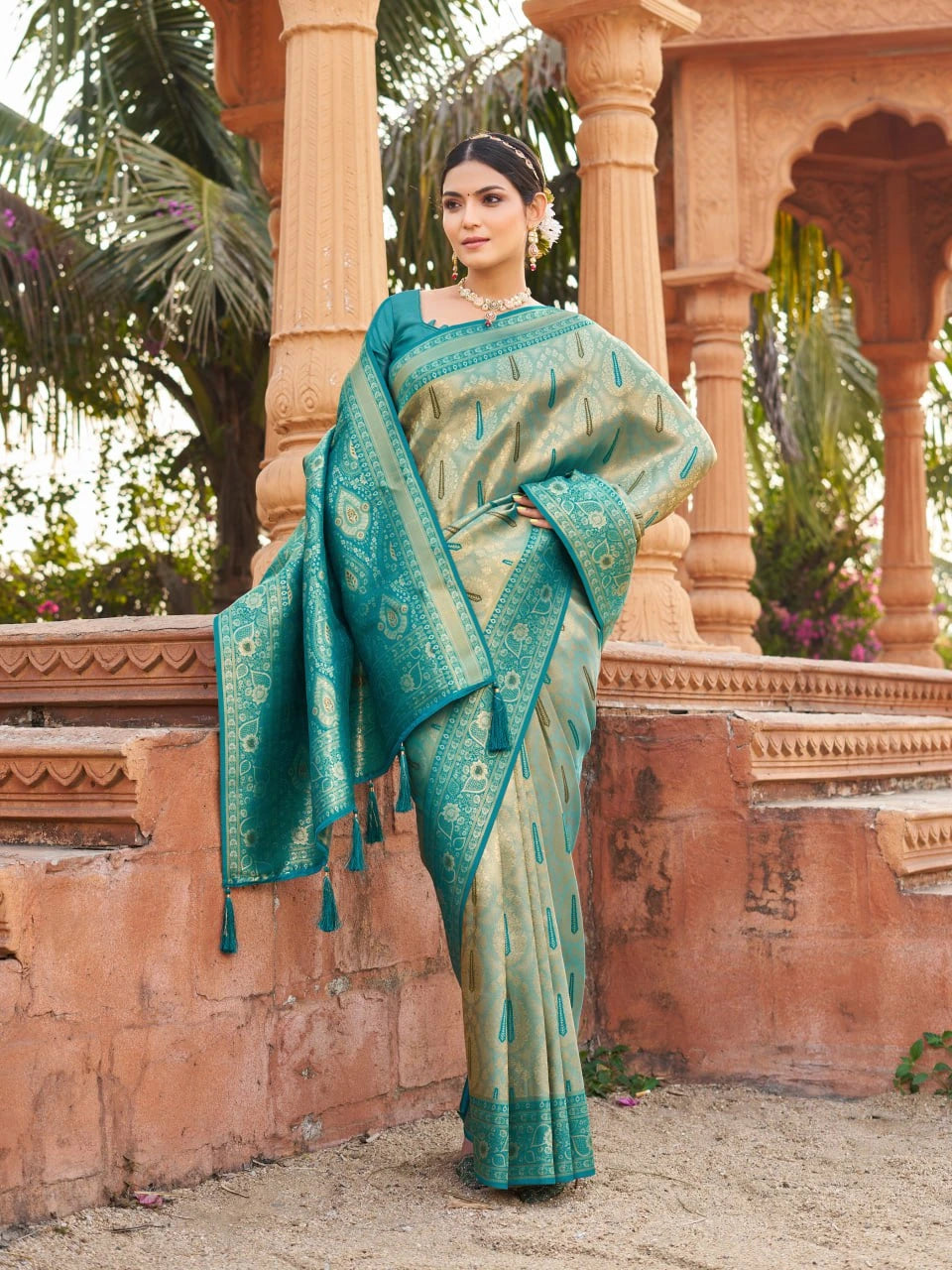 Woman in a teal saree standing in front of an architectural structure with columns.
