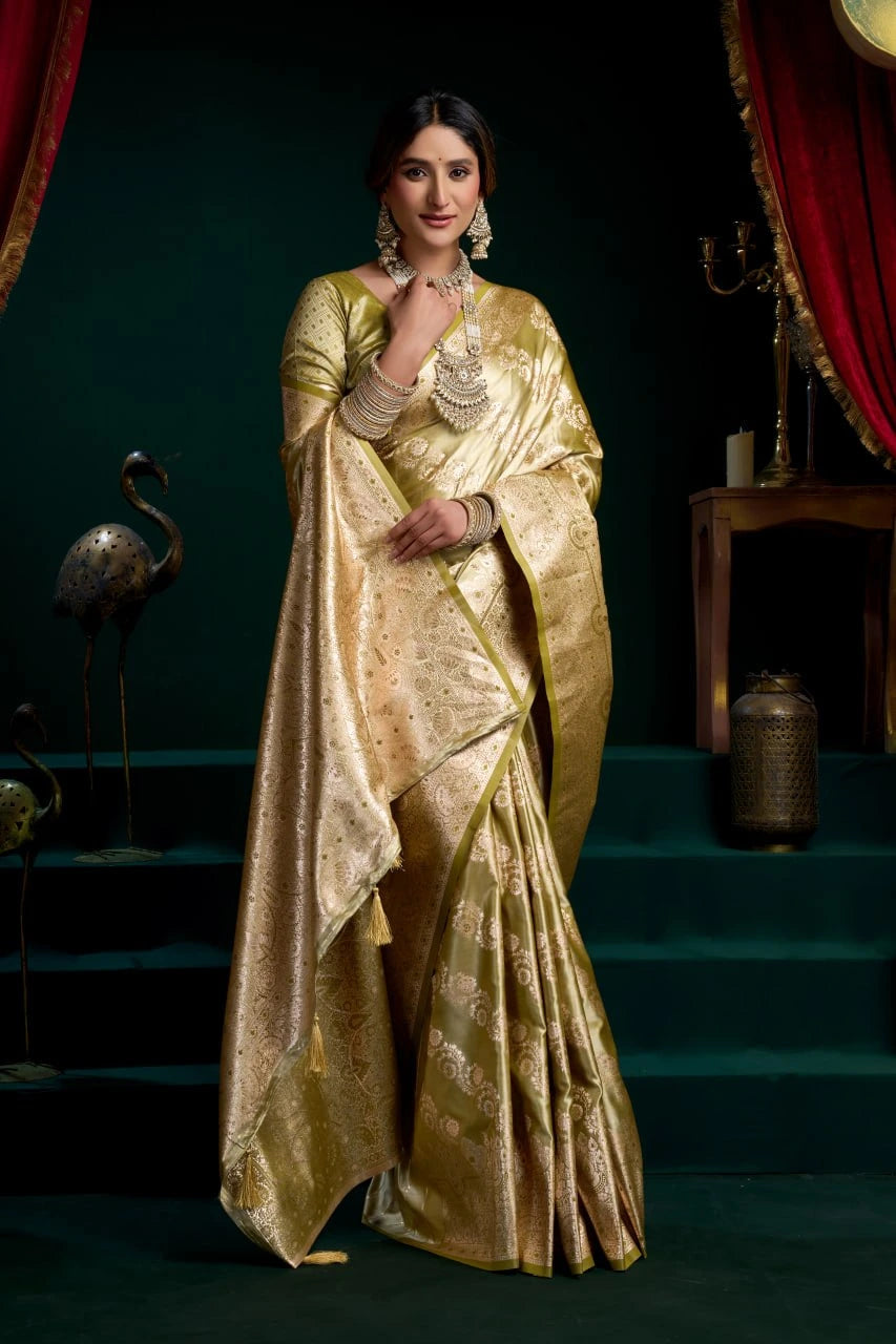 Woman in a gold saree standing in a decorative setting with red curtains and dark background.