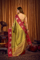 Woman in a green and red saree standing in front of a vintage gramophone and wooden cabinet.