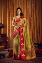Woman wearing a red and green saree with a gold border against a brown curtain background