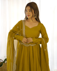 Woman wearing a mustard yellow traditional outfit with gold embroidery against a white curtain background