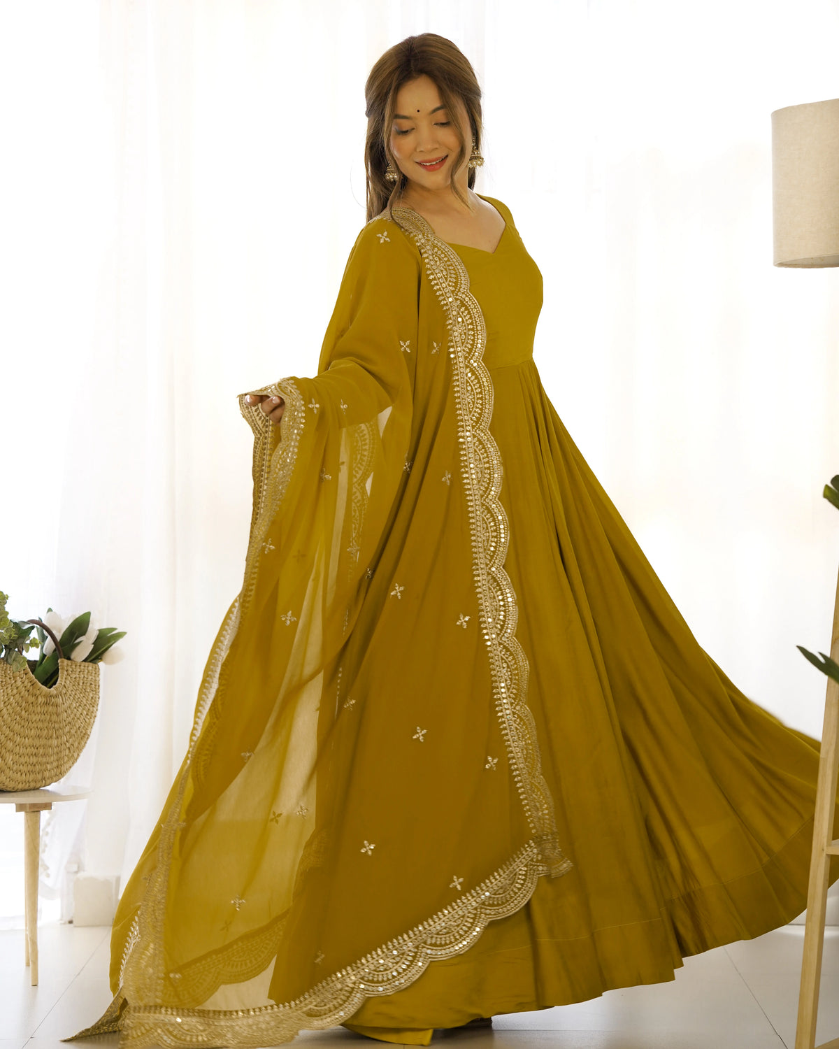 Woman wearing a mustard yellow dress with white embroidery in a bright room.