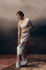 Woman in a white saree with floral patterns standing against a dark background