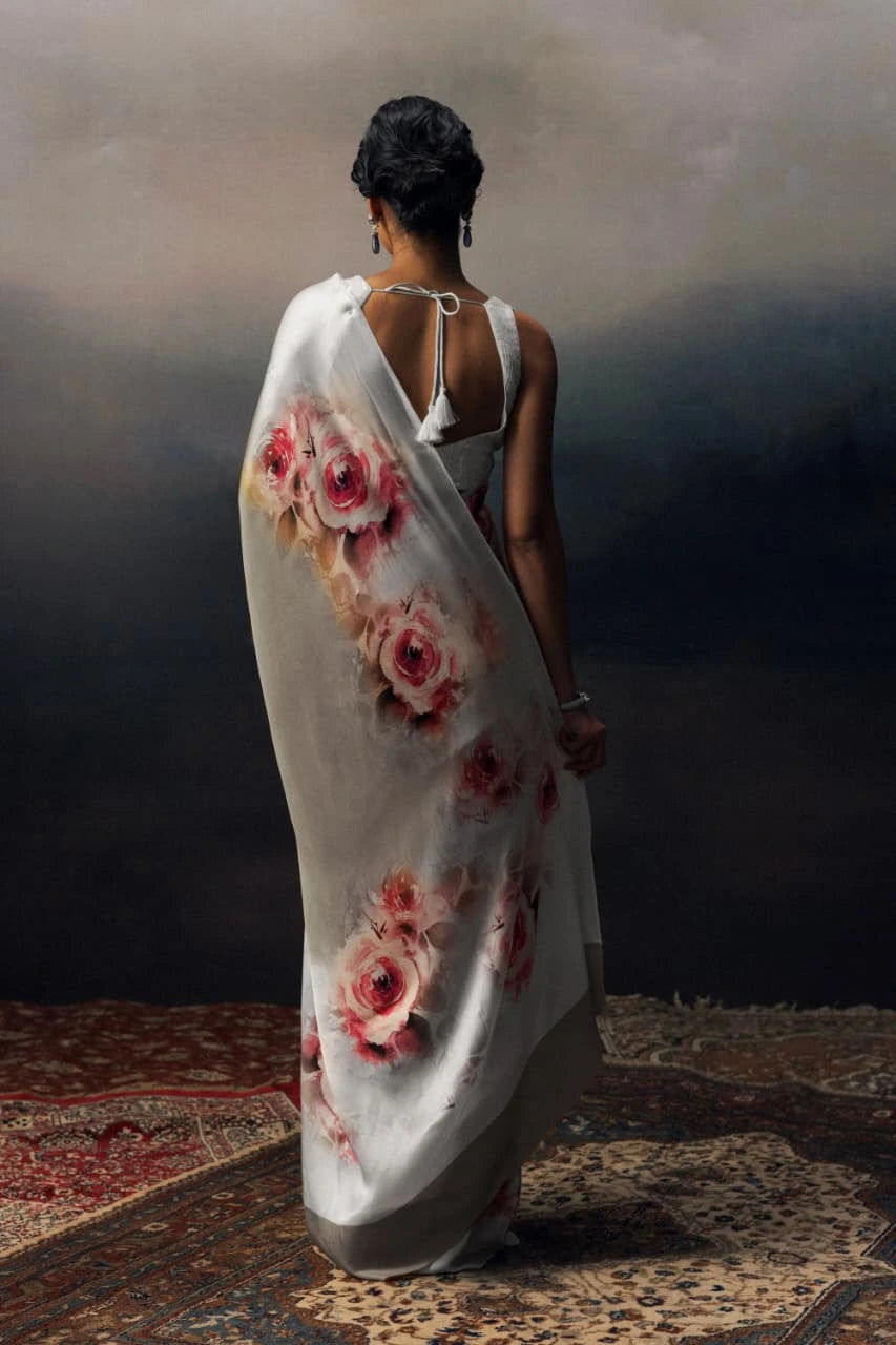 Woman holding a white saree with red floral patterns against a dark background