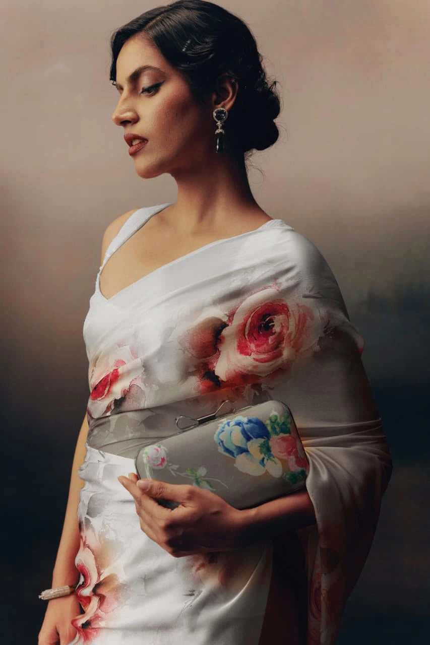 Woman wearing a floral saree with a matching clutch against a neutral background