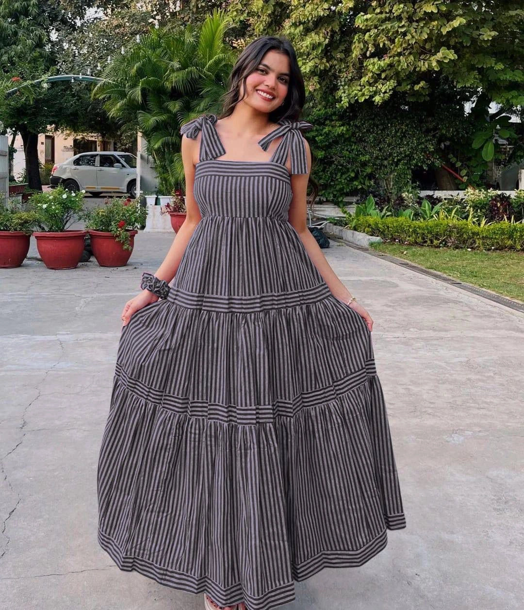 Woman in a striped dress standing outdoors with greenery in the background