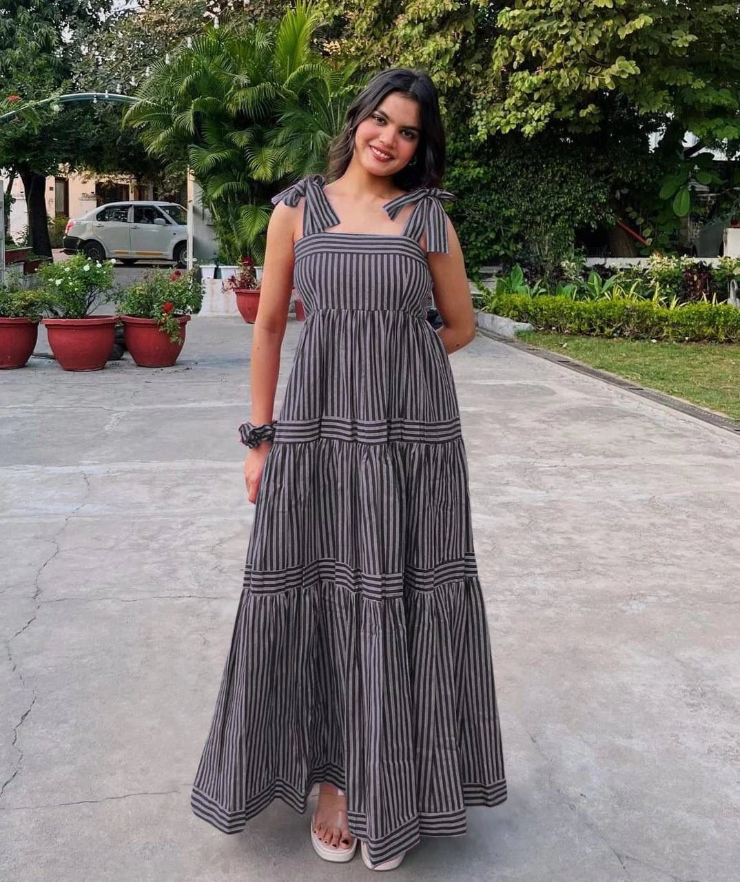 Woman in a long black and white striped dress standing on a paved path with greenery in the background.