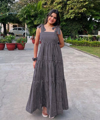 Woman in a long black and white striped dress standing on a paved path with greenery in the background.