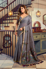Woman in a gray saree with floral patterns standing in a decorated room.