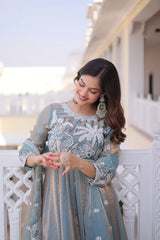 Woman in a light blue embroidered dress standing on a balcony.