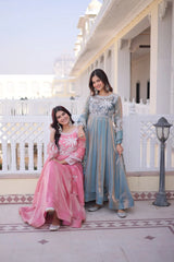 Two women in traditional outfits standing on a balcony with a white building in the background.