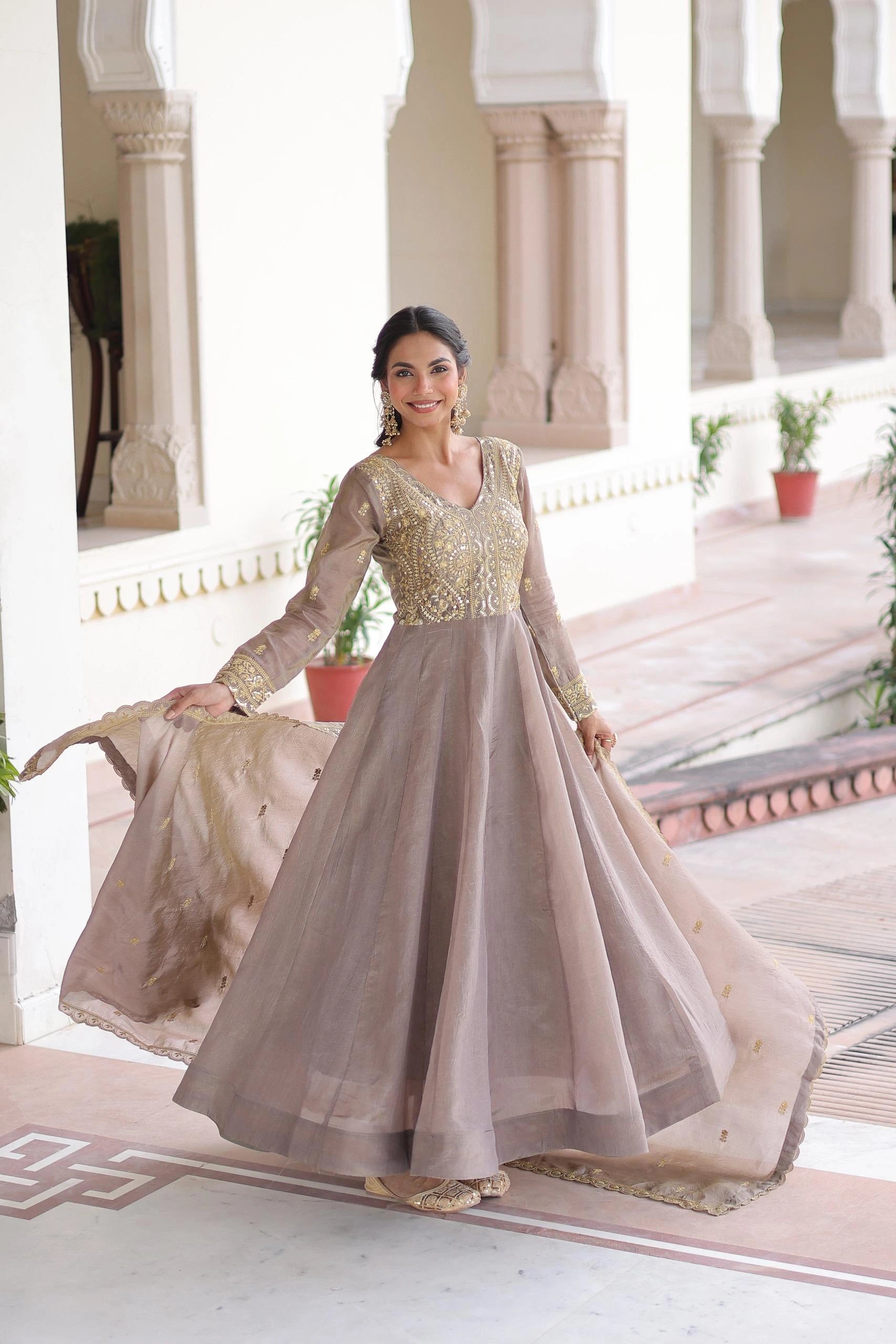 Woman in a traditional outfit standing in an elegant indoor setting with architectural columns.