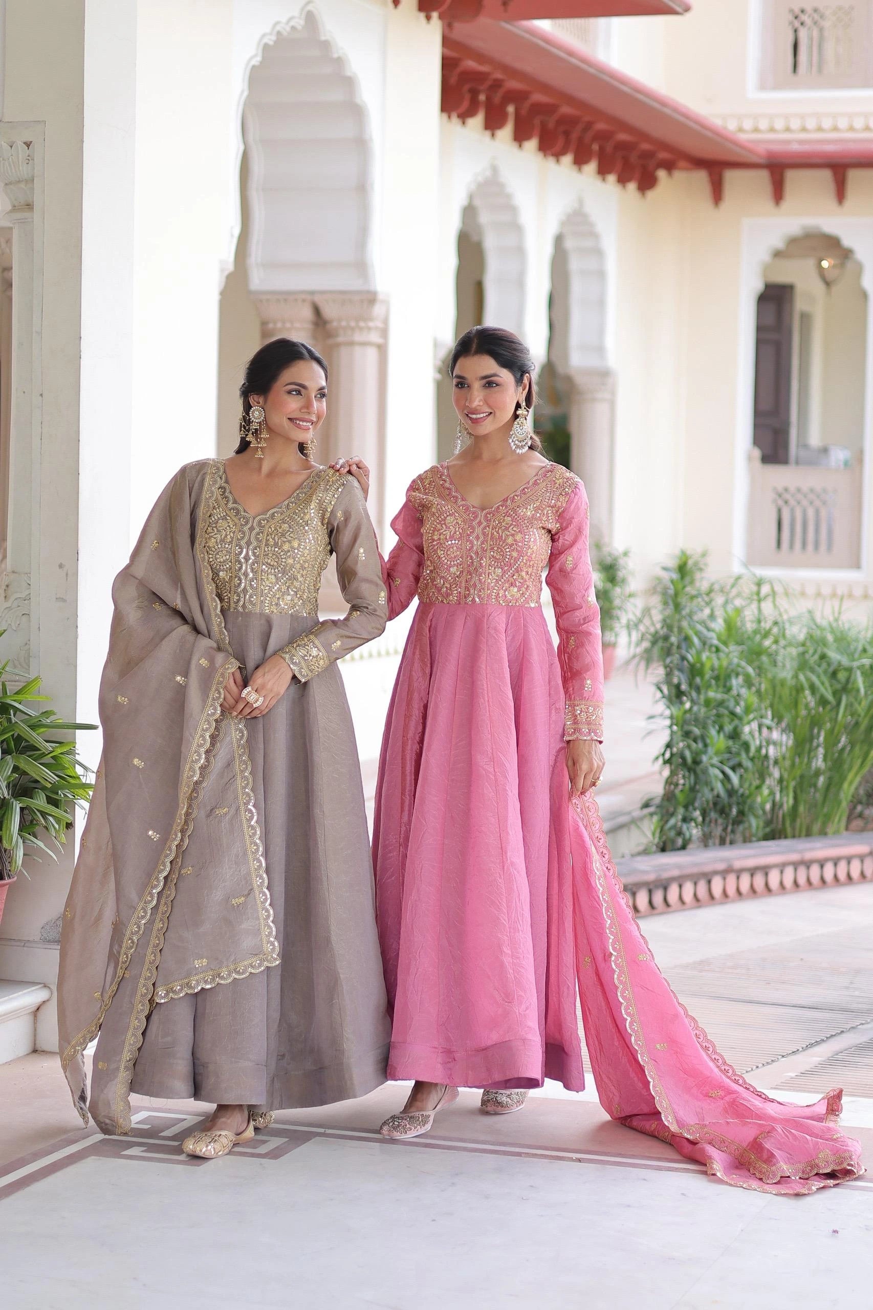 Two women in traditional outfits standing in a decorative outdoor setting.