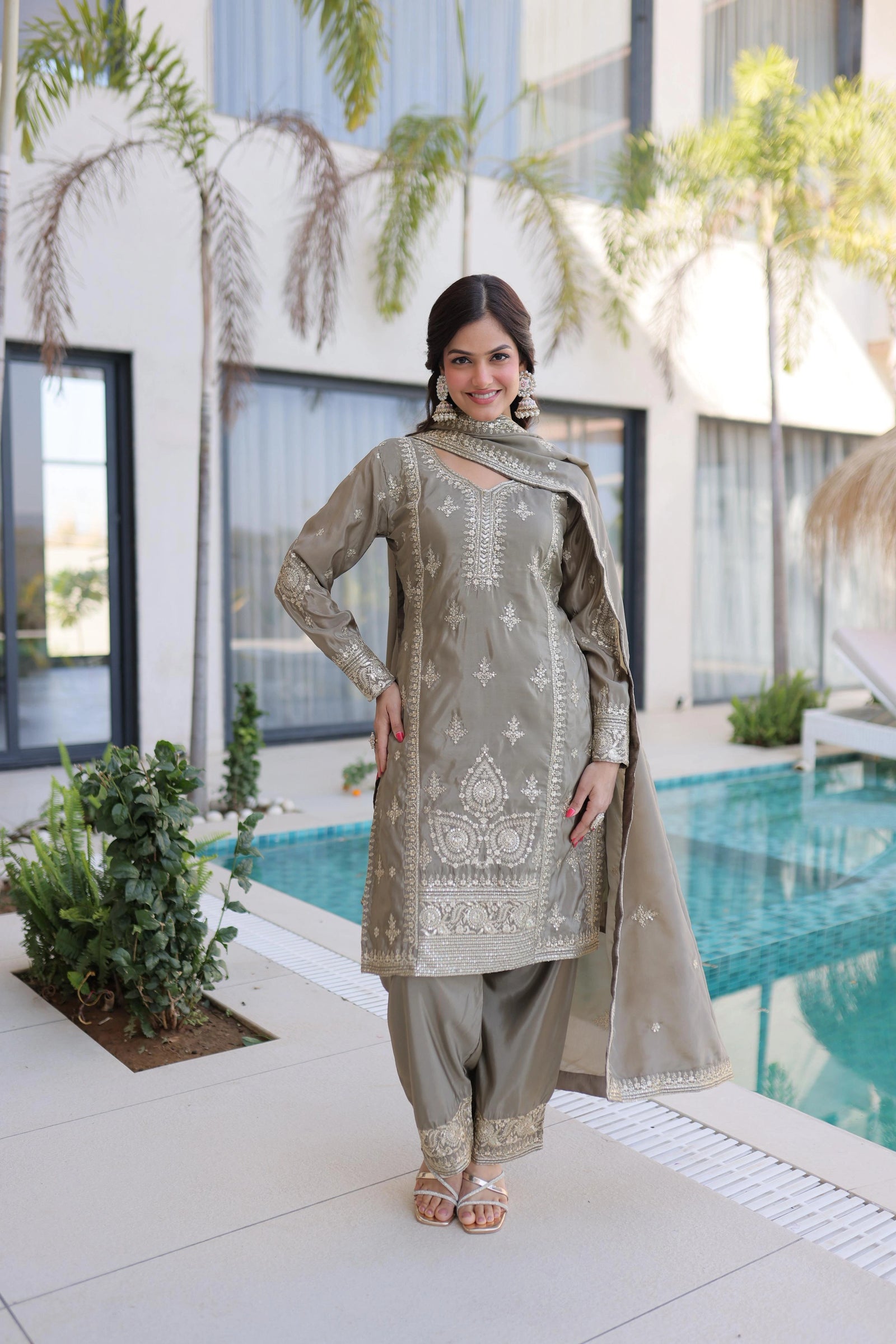 Woman in traditional outfit standing by a pool with modern building and greenery in the background
