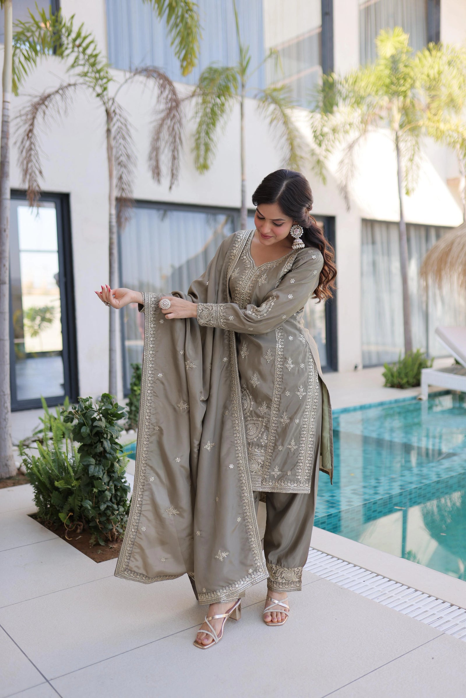Woman in a traditional outfit standing by a pool with a modern building in the background