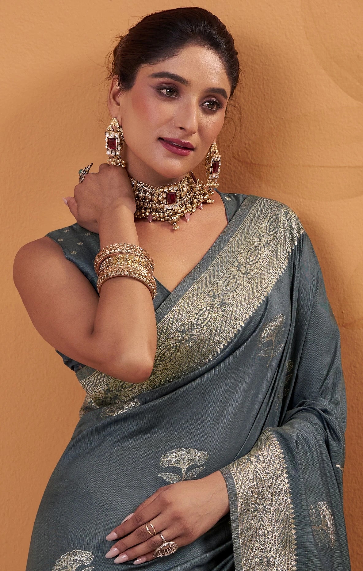 Woman in a gray saree with gold embroidery against a beige background