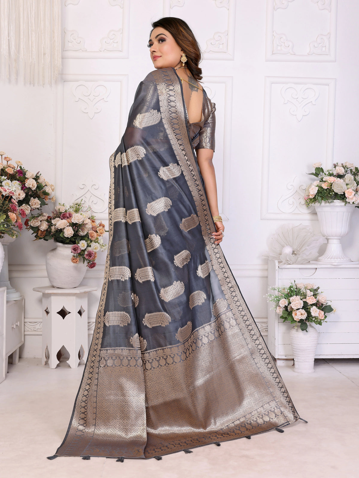 Woman wearing a gray saree with white patterns in a decorated room.