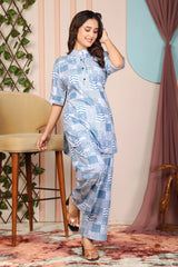 Woman wearing a blue patterned outfit standing in a room with decorative elements.